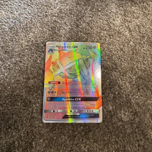 Metagross GX Pokémonkort - Säljer ett holografiskt Metagross GX Pokémonkort med färgstark regnbågseffekt. Kortet har 250 HP och flera attacker, inklusive Giga Hammer och Algorithm GX. Perfekt för samlare eller Pokémon-entusiaster.