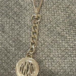 Guldfärgad nyckelring från DKNY - Säljer en guldfärgad nyckelring från DKNY med rund berlock där det står  DKNY-logga i mitten. Kedja och karbinhake i metall. Perfekt som accessoar till väskan eller nycklarna.