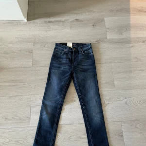 Mörkblå High Kai jeans från Nudie Jeans - Säljer ett helt nytt par mörkblå jeans från Nudie Jeans i modellen High Kai. Klassisk femficksdesign med snygga slitningar och vågig brodyr på bakfickan. Jeansen har normal passform och raka ben. Perfekta för dig som gillar stilrena jeans.