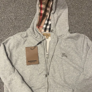  Burberry Grå hoodie med dragkedja. - Säljer en  grå hoodie zipupp från Burberry helt ny skick med tags på, perfekt för att få den dyra stilen. Den är i storlek M men den kan upplevas vara lite mindre så Alltså S/M men jag rekommenderar det för er som har S eller XS till och med. Pris kan vi självklart diskutera 🙌