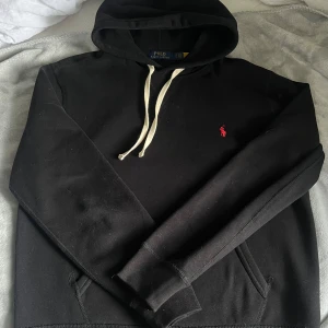 Ralph Lauren Hoodie Svart - Svart hoodie från Ralph Lauren, storlek M. Använd men i mycket fint skick. Tidlös design med klassisk Polo-logga på bröstet. Bekväm passform och mjukt material som gör den perfekt både till vardags och för en avslappnad stil. 
