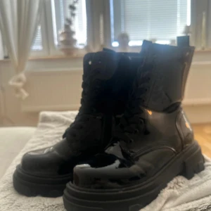 Svarta lackade boots med snörning - Säljer ett par chunky svarta boots i glansigt lackmaterial med grov sula och snörning hela vägen upp. Skorna här helt nya! 