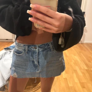 Blå jeans minikjol - Säljer en blå jeans minikjol med rå kant och slitning på ena sidan. Klassisk femficksmodell med knapp och dragkedja framtill. Perfekt för dig som gillar en trendig och avslappnad stil. Vet inte märke tyvärr💖