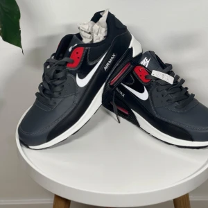 Nike Air Max svart och röd - Säljer ett par Nike Air Max sneakers i svart med röda och vita detaljer. Skorna har klassisk Air Max-sula, vit swoosh och svarta skosnören. Perfekta för dig som gillar sportig stil och vill ha bekväma sneakers med snygg design.
