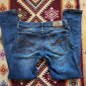 Nudie Jeans Gim Tim - Säljer ett var blåa grim tim jeans från Nudie Jeans med snygg tvätt, slim passform och raka ben. Jeansen har fem fickor, knappgylf och snygga slitningar framtill. W30 L32.