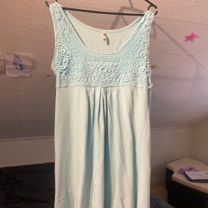 Ljusblå ärmlös klänning med virkad överdel från Flash - Säljer en ljusblå ärmlös klänning från Flash med vacker virkad detalj upptill. Klänningen har rund halsringning och ett mjukt, fallande tyg nedtill. Perfekt för varma dagar och enkel att styla.