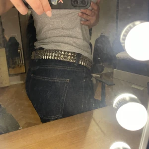 Svart nitarbälte med silverdetaljer - Säljer ett svart bälte med silvriga fyrkantiga nitar och metallspänne. Bältet är brett och har en cool, rockig stil som passar perfekt till jeans. Materialet är skinnimitation och nitarna ger ett extra edgy uttryck.