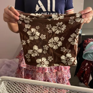 Brun blommig kjol från H&M Divided - Supersöt brun topp  med vita blommor från H&M Divided. Toppen  har ett blommigt mönster och är i en kort modell, perfekt för varma dagar. Mjuk och lätt att bära, passar dig som gillar en avslappnad och trendig stil.