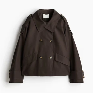 H&M trenchcoat  - Säljer en brun oversized trenchcoat med dubbelknäppning och stora slag. Jackan har långa ärmar med knappar vid ärmslut och axelklaffar. Jackan är helt slutsåld på H&m och super populär. Köptes för 600 kr! Denna jacka passar perfekt nu till våren! Den sitter som en L, för var ganska liten i storlek