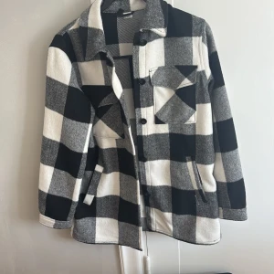Svartvit rutig jacka  - Säljer en oversized overshirt i svart och vitt med stora rutor. Jackan har knappar framtill, bröstficka och två sidofickor.