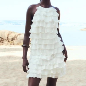 Vit volangklänning med halterneck - Supersöt vit miniklänning med volanger och halterneck. Klänningen har öppen rygg med knytband och är perfekt för till exempel studenten! Aldrig använd. Helt slutsåld på hemsidan. 