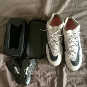 Nike Zoom fotbollsskor grå och svart med svarta monolit benskydd  - Säljer ett par vita Nike Zoom fotbollsskor med svart svarta monolit benskydd. Skorna har snörning och är designade för bra grepp på planen. Perfekta för dig som vill ha lätta och snabba skor till match eller träning.                                            Skorna kommer med en låda och är super bra condition använd 5 gånger. Storlek 45