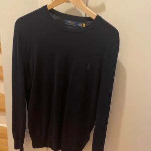 Marinblå stickad tröja från Polo Ralph Lauren - Klassisk marinblå stickad tröja från Polo Ralph Lauren med rund halsringning och diskret broderad logga på bröstet. Perfekt för en stilren och enkel look. Långärmad modell med mjukt material. Nypris 1799kr