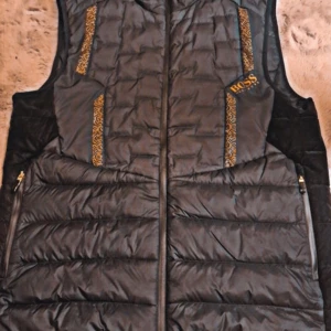 Svart dunväst från Hugo Boss - Snygg svart dunväst från Hugo Boss med gulddetaljer och dragkedja framtill. Västen har quiltad design och två fickor med dragkedja. Märkeslogga i gult på bröstet och dekorativa mönsterband längs sidorna. väldigt sällsyn väst köptes för 3000 men gillade inte den så mycket och inte använd så mycket säljer den snabbt för ska flytta kan gå ner i pris bara skriv 