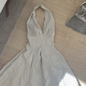 Vit halterneckklänning med svarta prickar - Säljer en vit halterneckklänning med svarta prickar och djup v-ringning. Klänningen har en utställd kjol och bandet går runt nacken. Säljer då den inte kommer till användning❤️❤️