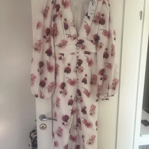 Blommig långklänning med ballongärmar från Gina Tricot - Superfin långklänning från Gina Tricot med blommigt mönster i rosa och vinröda toner. Klänningen har djup v-ringning, markerad midja, knappar framtill och ballongärmar. Prislapp kvar, endast provad!