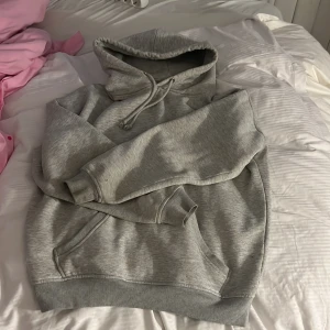 Grå hoodie från Bik Bok - Säljer en klassisk grå hoodie från Bik Bok i storlek S. Tröjan har huva med dragsko och en stor magficka framtill. Perfekt för en avslappnad stil och enkel att matcha med det mesta.