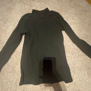 Svart ribbad polotröja - Säljer en svart ribbad polotröja med lång ärm. Tröjan har en tight passform och är perfekt för lager-på-lager. Enkel och stilren design som passar till det mesta.