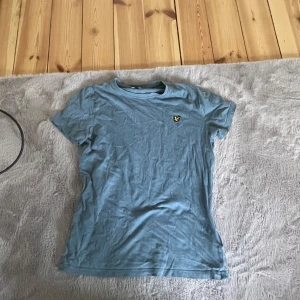 Blå t-shirt från Lyle & Scott Junior - Säljer en ljusblå t-shirt från Lyle & Scott Junior med klassisk passform och korta ärmar. T-shirten har en liten broderad logga i gult på bröstet. Perfekt basic till garderoben!