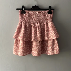 Rosa blommig volangkjol från Seaside 💕 - Supersöt rosa kortkjol från Seaside med vita småblommor och två lager volanger. Kjolen har smock i midjan för extra bekväm passform och är perfekt för vår och sommar. 💕