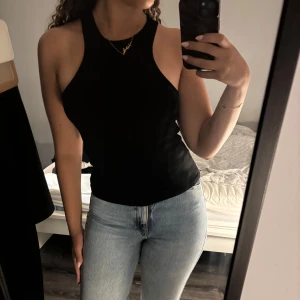 Svart linnetopp från Gina Tricot - Säljer en stilren svart linnetopp från Gina Tricot. Toppen har en enkel design med ärmlös skärning och rund hals. Perfekt för en minimalistisk look.