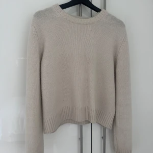 Beige stickad tröja i ull/kashmir H&M - Beige stickad tröja från H&M i en mjuk ull- och kashmirblandning. Modellen är croppad med ribbade muddar vid ärmslut, nederkant och halsringning. Perfekt för lager-på-lager och enkel att matcha med jeans eller kjol.