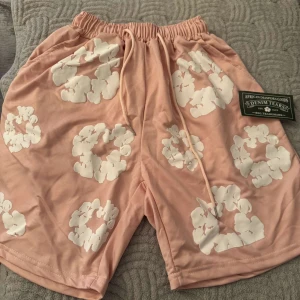Rosa blommiga shorts från Denim Tears - Snygga rosa shorts från Denim Tears med vita blommiga mönster. Dom är oanvända. Storlek M