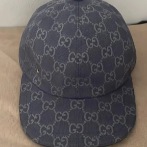 Gucci keps med GG-mönster - Snygg keps från Gucci i mörkblått tyg med det klassiska GG-monogrammet över hela kepsen. Kepsen har böjd skärm och justerbar passform. Materialet är tåligt och har en exklusiv känsla, perfekt för dig som vill sticka ut med en ikonisk accessoar.