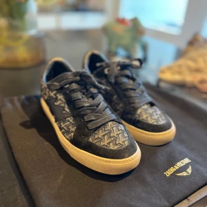 Zadig & Voltaire skor - Snygga svarta sneakers från Zadig & Voltaire med coolt mönster i grått och svart. Skorna har snörning, rund tå och vit platt sula. Ovandelen är i textil och skinn med ett grafiskt mönster som ger en unik vibe. Perfekta för dig som vill sticka ut med stilen.