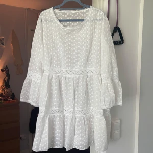Vit broderad sommarklänning med volang - Superfin vit klänning med broderade småblommor och spetsdetaljer. Lätt och luftig modell med volanger och trekvartsärmar. Perfekt för varma dagar och har en romantisk vibe. Tillverkad i bomull för extra komfort.