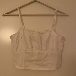 Vit linnetopp  - Säljer en söt vit linnetopp från H&M Divided i storlek XS. Toppen har smala axelband, rynkade detaljer upptill och en lätt croppad passform. Perfekt till sommaren och enkel att matcha med jeans eller kjol.