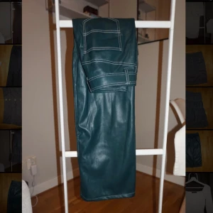 Mörkgröna skinnbyxor med kontrastsömmar - Snygga mörkgröna byxor i skinnimitation med raka ben och vita kontrastsömmar. Klassisk femficksmodell med bälteshällor och dragkedja fram. Perfekt för dig som vill sticka ut med en cool look.