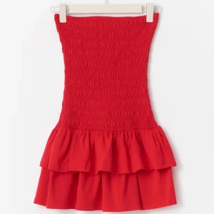 Röd axelbandslös volangklänning - Superfin röd kortklänning med smockad överdel och dubbla volanger nertill i storlek XS. Axelbandslös modell som sitter tight upptill och har en luftig kjol. Perfekt för dig som vill sticka ut med en färgstark look i sommar. Använd en gång!