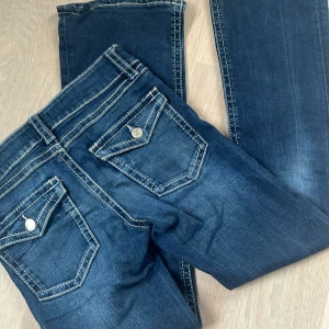 Blå jeans från Gina Tricot, stl 152 - Snygga blå jeans från Gina Tricot med kontrastsömmar och coola fickdetaljer med lock och knapp bak. Klassisk femficksmodell i stretchig denim som sitter skönt och har en modern look.