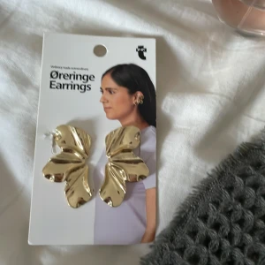 Stora guldiga örhängen i bladform - Säljer ett par statement örhängen i blankt guldigt metall med snygg bladformad design. Perfekta för dig som vill sticka ut och ge din look en cool touch. Säljs på originalkortet.