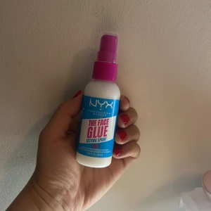 NYX The Face Glue Setting Spray - NYX The Face Glue Setting Spray i en smidig vit plastflaska med blå etikett och rosa spraykork. Innehåller 60 ml. Perfekt för att fixera sminket och hålla looken på plats hela dagen. Lätt att använda med praktisk sprayfunktion.