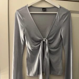 Ljusblå omlottopp med knyt från Gina Tricot - Supersnygg ljusblå omlottopp från Gina Tricot med lång ärm och djup v-ringning. Toppen har knyt framtill som ger en trendig look och sitter tajt över kroppen. Perfekt att styla med jeans eller kjol för en cool vibe.