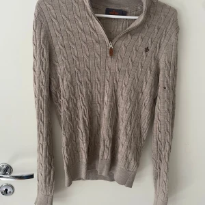 Beige kabelstickad half zip från Morris - Kabelstickad beige tröja från Morris med half zip och lång ärm. Tröjan har en klassisk kabelstruktur, ribbade muddar och liten broderad logga på bröstet. Perfekt för lager-på-lager och snygg till jeans eller chinos. Tröjan har däremot 2 små hål som ni kan se på bilderna men dom syns inte så mycket. Nypris 1700kr mitt pris 449kr