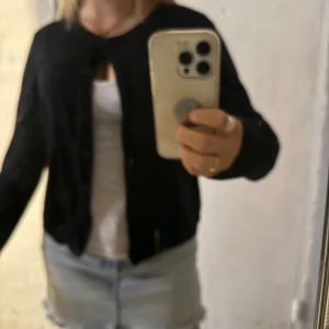 Svart cardigan jacka med knappar - En svart cardigan jacka med rund hals och knäppning framtill. Jackan är långärmad och har ribbade muddar vid ärmslut och nederkant. Perfekt att slänga över ett linne eller t-shirt för en chill look. Väldigt liten i storleken och passar mig med xs.
