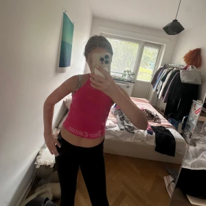 Juicy Couture rosa croppad linnetopp - Juicy Couture croppad linnetopp i stark rosa med vit logga längs nederkanten. Toppen är ärmlös och har en tight passform, perfekt för dig som gillar en sportig och trendig look. Mjuk och stretchig i materialet.