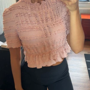 Ljusrosa volangtopp - Supersöt ljusrosa topp korta ärmar och volangdetaljer över hela toppen. Croppad modell med sturktur i tyget. Har aldrig kommit till användning, därav säljer jag den. Jag fick den i present och den är i storlek S, supersöt och oanvänd! 🎀💕
