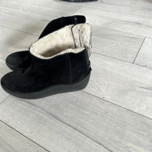 Svarta boots från Catwalk med foder - Svarta boots från Catwalk med mjukt vitt foder och dragkedja på sidan. Skorna har en rund tå, platt sula och är tillverkade i mocka. Perfekta för kyliga dagar med sin varma insida och stilrena look.