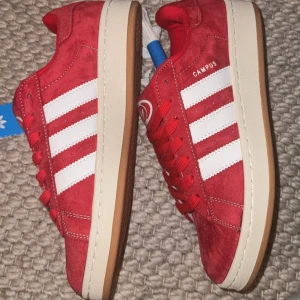 Röda Adidas Campus sneakers mocka - Snygga röda Adidas Campus sneakers i mocka med klassiska vita ränder på sidorna och vit logga på plösen. Skorna har röda snören, vit mellansula och gummisula i brunt. Perfekt för dig som vill sticka ut med en retrostil. Unisex (Zalando) oanvända 