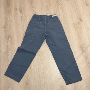 Snygga blåa skate chinos från butter  - Snygga blå chinos med raka ben och avslappnad passform. Byxorna har snörning i midjan för extra komfort och två bakfickor med diskreta detaljer. Perfekta för en chill och stilren look.