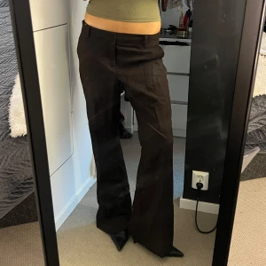 Bruna kostymbyxor  - Snygga bruna kostymbyxor från Gina Tricot med klassisk passform och vida ben. Byxorna har hällor för bälte, diskreta fickor och stängs med dragkedja och knapp. Perfekta för en clean och stilren look.