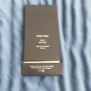 Tom Ford Oud Wood EdP 100ml - Lyxig parfym från Tom Ford, Oud Wood Eau de Parfum i 100 ml flaska. Flaskan är svart och har en elegant, fyrkantig design med silverdetaljer och tydlig logga. Kommer i en snygg mörkgrå ask med diskret mönster. Perfekt för dig som gillar exklusiva dofter, Oanvänt.