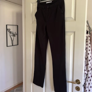 Svarta kostymbyxor med raka ben - Snygga svarta kostymbyxor med klassisk rak passform och diskreta fickor fram. Perfekta för en clean och stilren look. Byxorna har hällor för bälte och stängs med knapp och dragkedja.