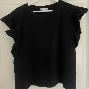 Volangtopp Zara - En svart topp/t-shirt från Zara med volangdetaljer längs axlarna. Säljer då jag inte använder den, endast använd 1 gång💞