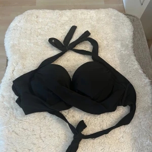 Svart bikiniöverdel med knyt - Snygg svart bikiniöverdel med vadderade kupor och breda knytband både i nacken och runt ryggen. Enkel och stilren design som passar perfekt till stranden eller poolen. Bekväm passform och klassisk look. Har bara använt den när jag solat 3-4 ggr