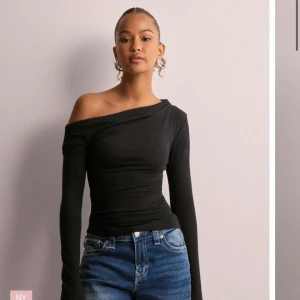 Svart offshoulder topp med lång ärm - Säljer en svart långärmad topp med offshoulder-design och tight passform. Toppen har en asymmetrisk halsringning som visar ena axeln och är tillverkad i ett mjukt, stretchigt material. Perfekt för dig som gillar en stilren och trendig look.